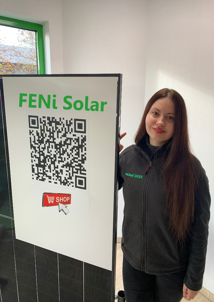 Junge Frau mit langen dunklen Haaren lächelt freundlich und steht neben einem FENi Solar QR Code